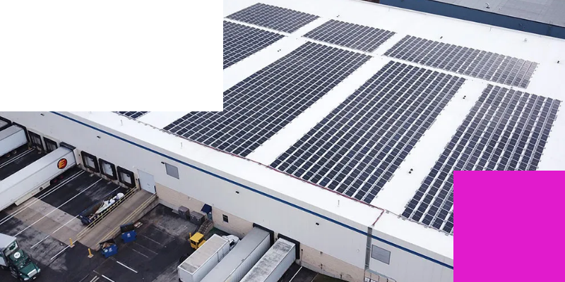 Aerial view of a warehouse with solar panels covering the roof and delivery trucks parked at loading docks.