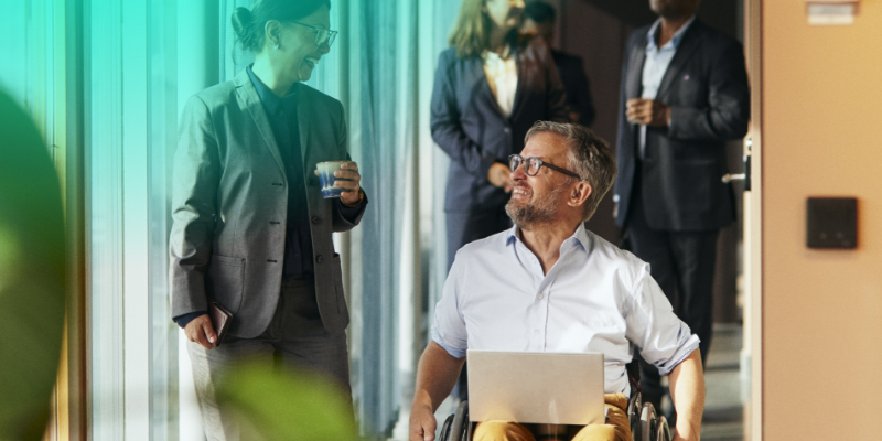 A man using a wheelchair speaking with a colleague outside an office building.