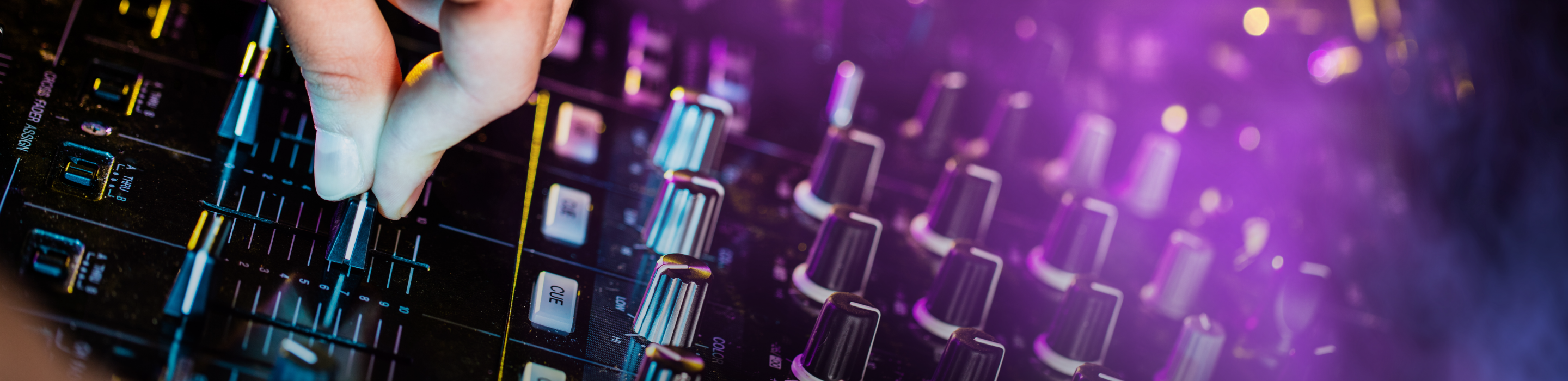Hand adjusting fader on DJ audio mixer with purple lighting.