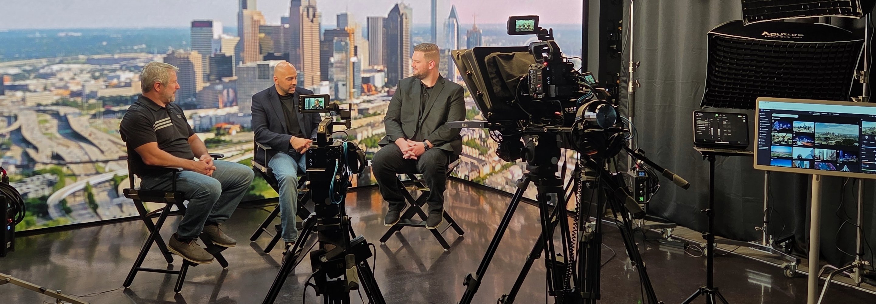 Three people filmed in studio with Atlanta skyline backdrop, cameras and lights visible.
