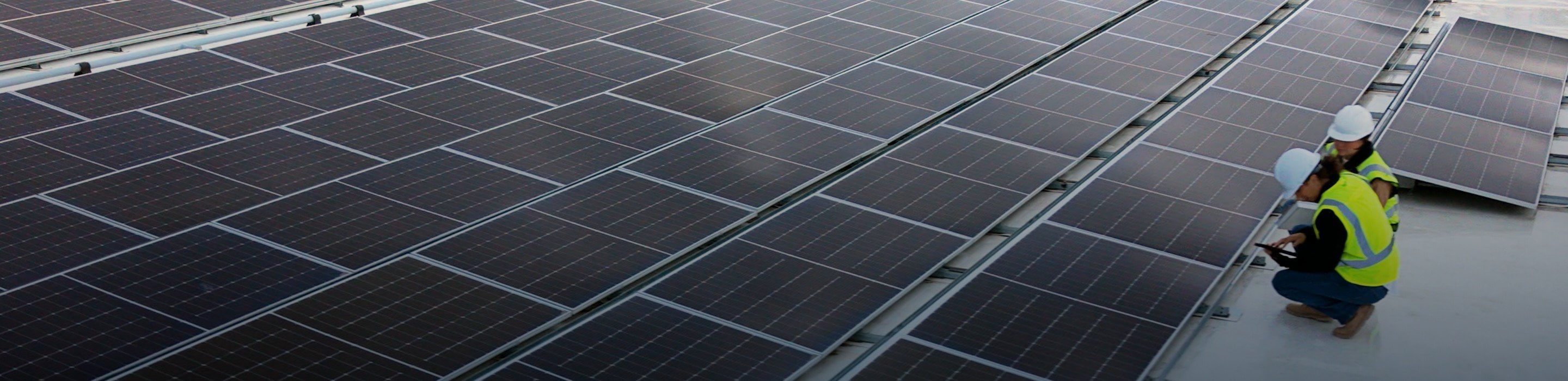 Worker in safety vest and hard hat inspecting solar panels on a large rooftop solar installation.