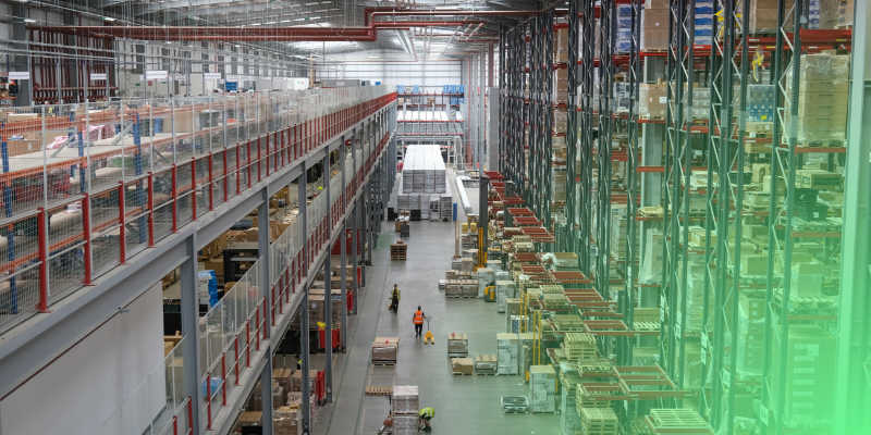 Modern warehouse with tall shelving, mezzanine, and workers in safety vests.