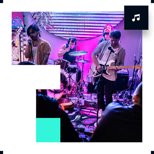 Band performing indoors with colorful lighting and audience watching.