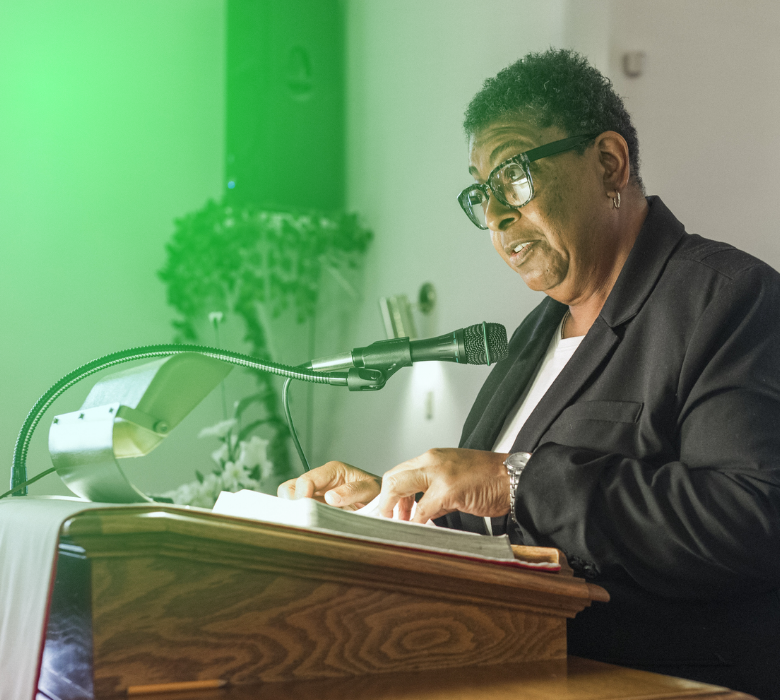 Person in glasses speaking at podium with microphone and book.