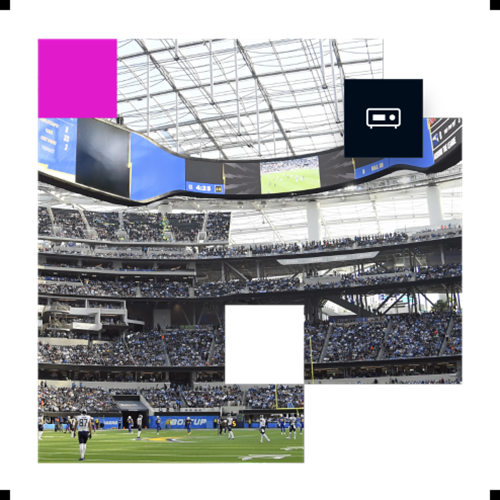 Indoor football stadium with a large video board and players on the field during a game.