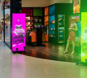 Clothing store entrance with bright digital advertising screens and mannequins.